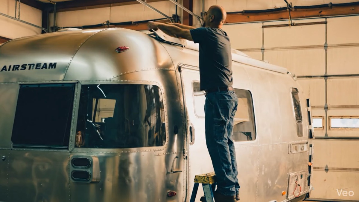 Illustrative scene of a man working beside an Airstream on a ladder